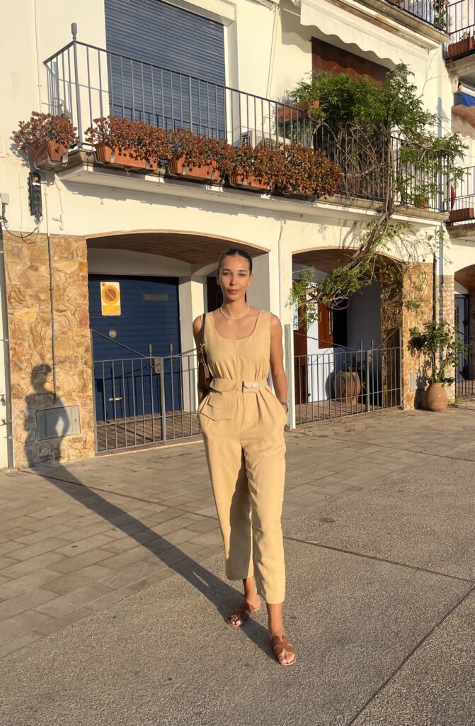 Girl standing wearing a beige set with brown sandals, beautiful outfit for summer and a sleek bun